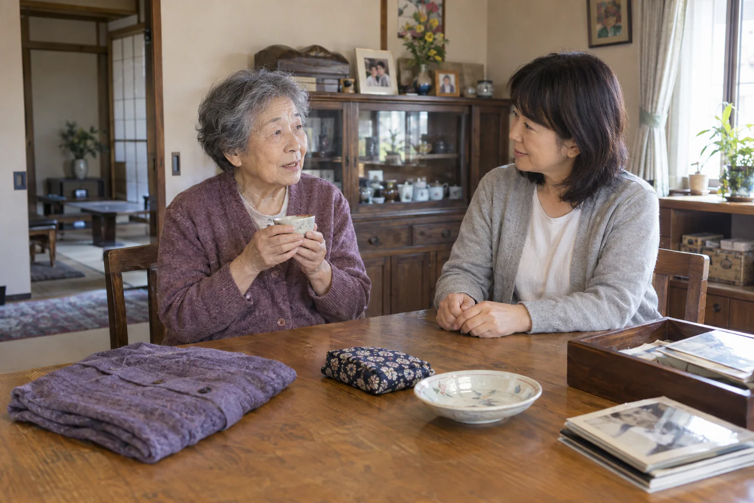 自宅の木のテーブルで、湯のみを手にした母親と娘が残したい品について話す場面